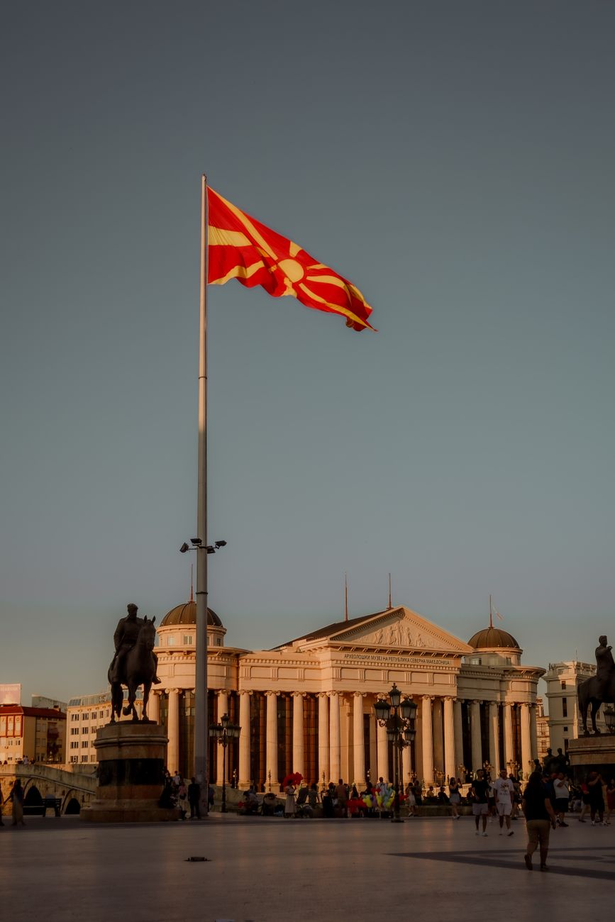 Nordmakedoniens flagga framför det neoklassiska Arkeologiska museet i Skopje vid solnedgången.