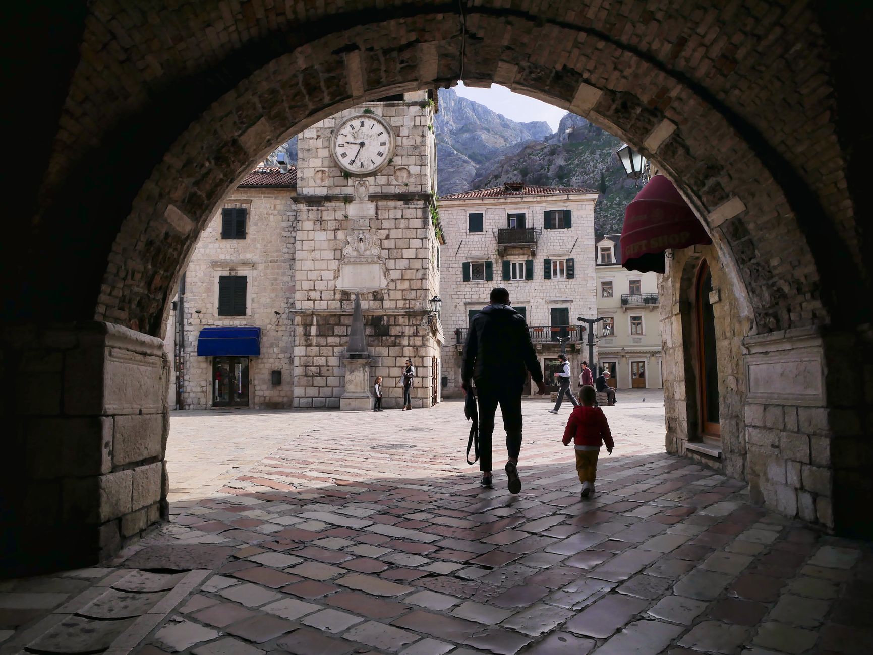 En vuxen och ett barn promenerar genom ett historiskt valv i gamla staden i Kotor, Montenegro.