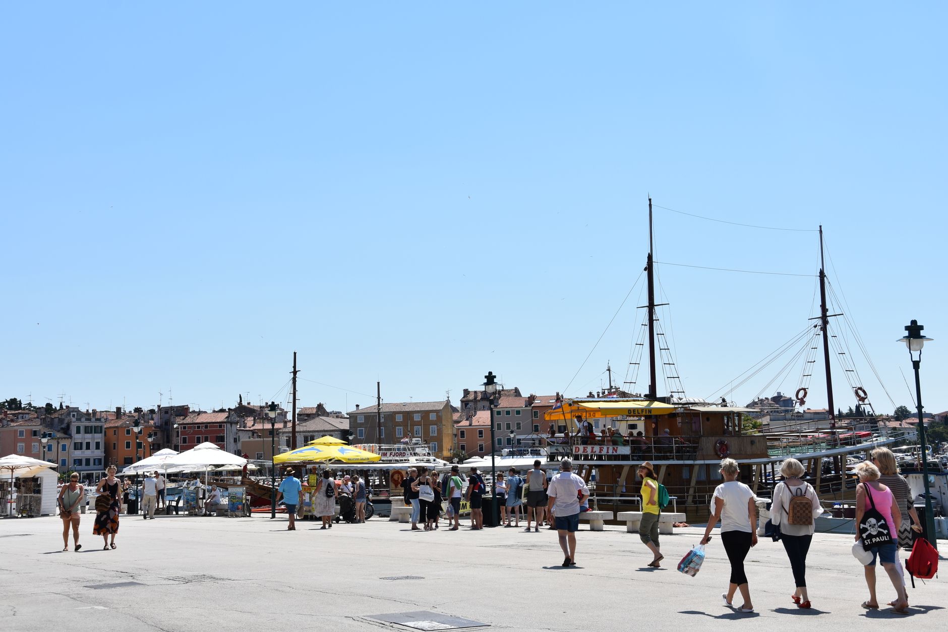 Människor på strandpromenaden i Rovinj under en klarblå himmel.
