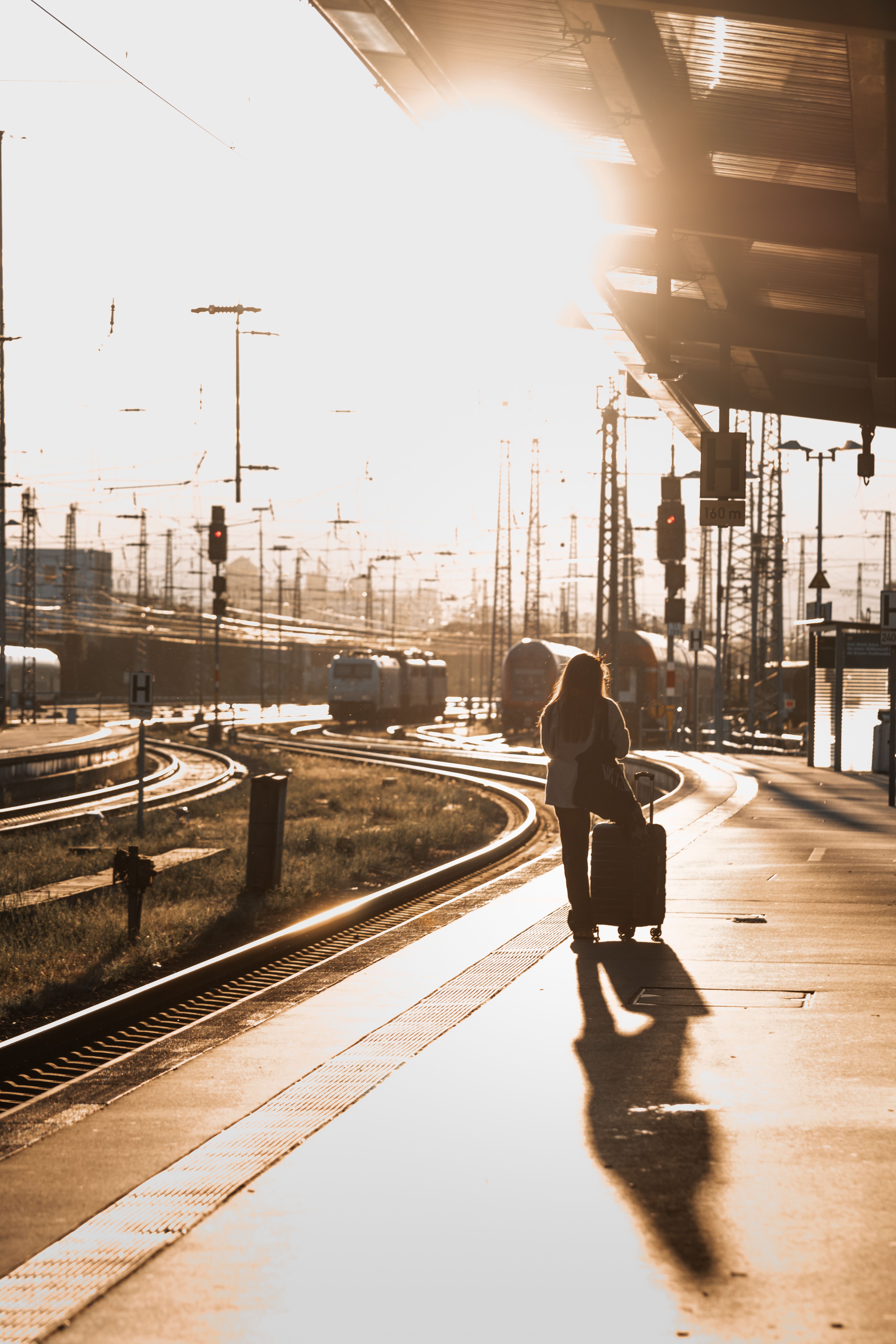 Kvinna med resväska står på en järnvägsstation i solnedgång.