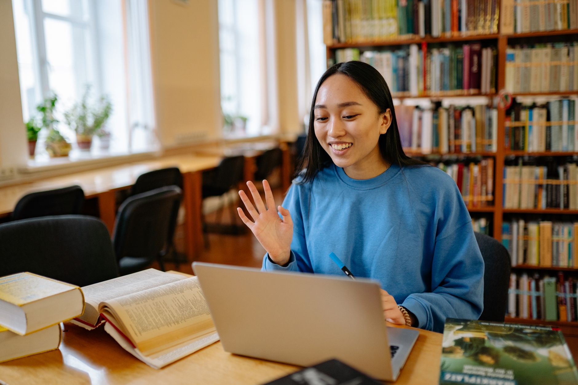 En leende student sitter med en bärbar dator i ett bibliotek.