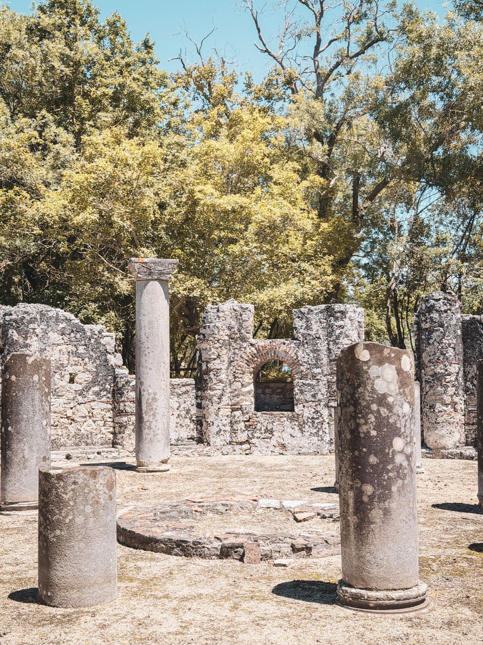 Ruiner med stenkolonner och murar omgivna av träd i Butrint i södra Albanien.