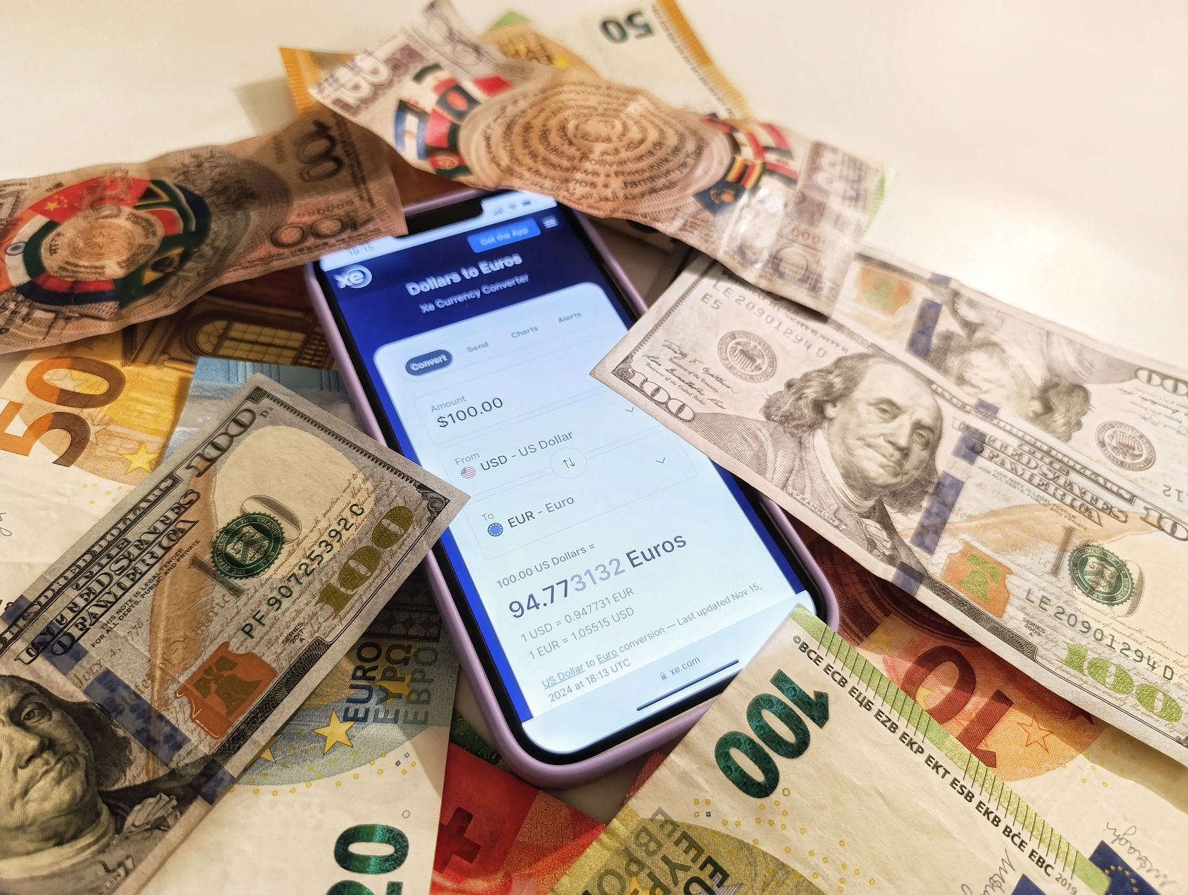 Mobiltelefon med en valutaomräknare på skärmen, omgiven av sedlar.