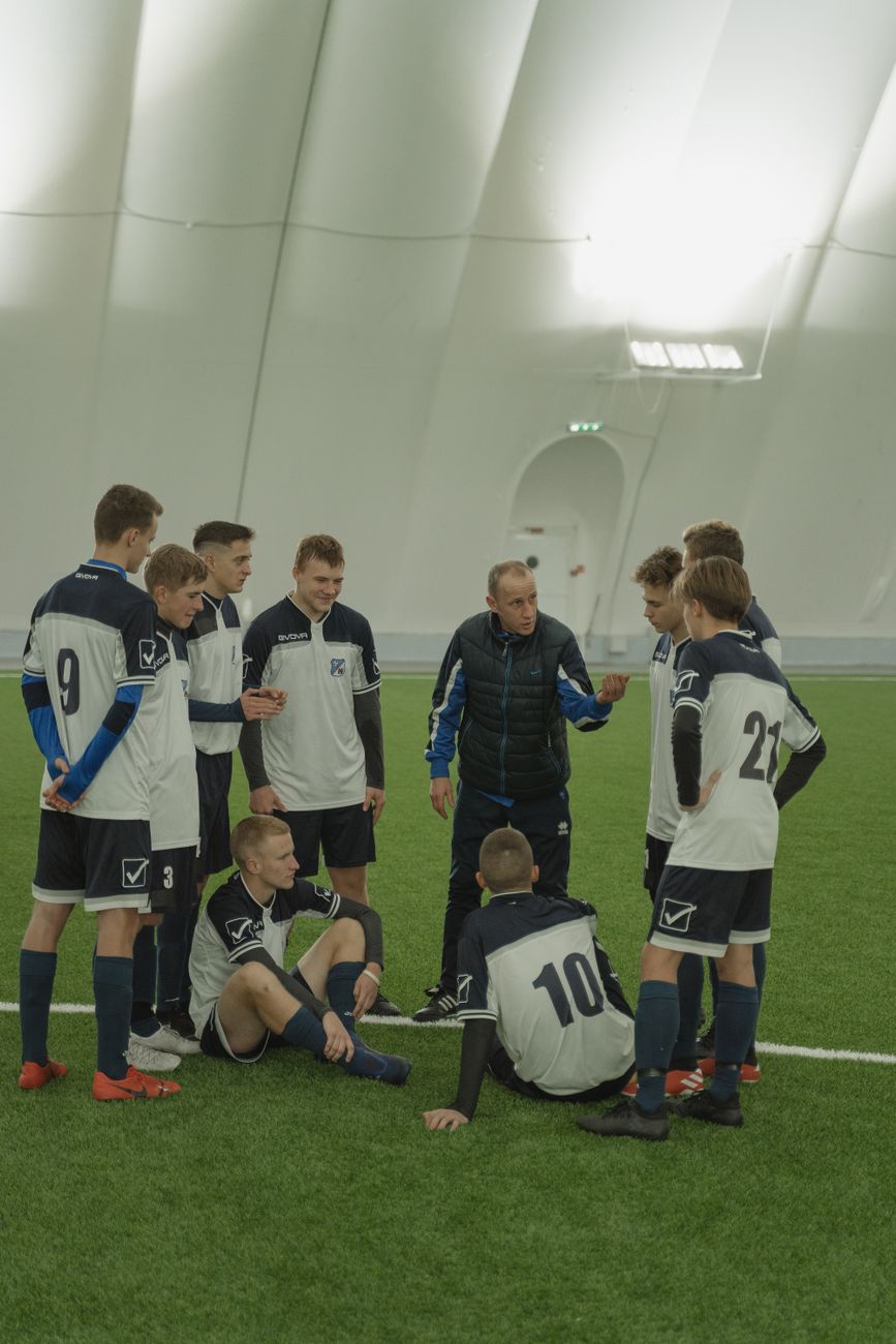 En tränare ger instruktioner till ett ungt fotbollslag inne i en sporthall.