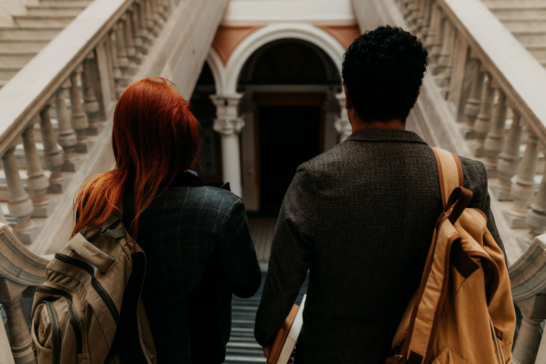 Två studenter med ryggsäckar går nerför en trappa i en historisk universitetsbyggnad