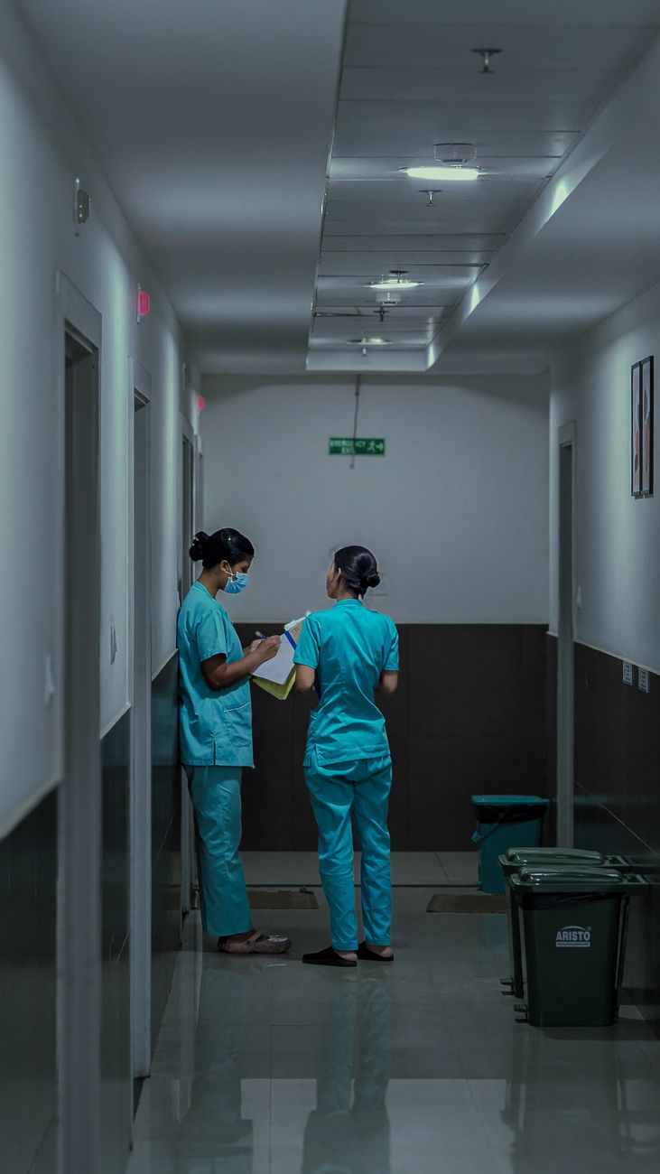 Två sjuksköterskor i vårdkläder går igenom patientanteckningar tillsammans i en sjukhuskorridor.