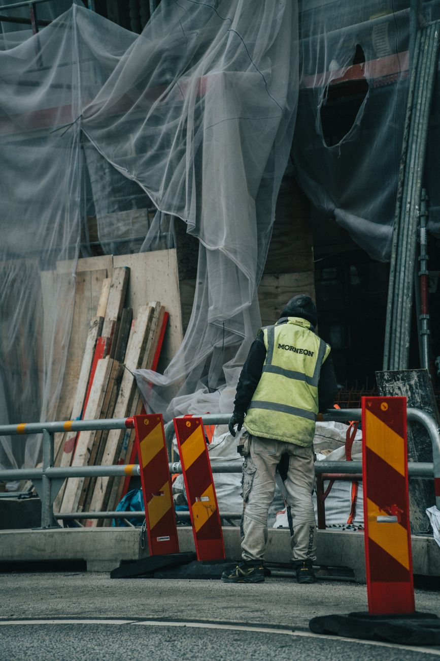 En byggarbetare i reflexväst och hjälm står vid en byggställning.